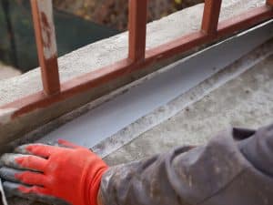 Worker applying waterproofing material to prevent leaking balconies in an outdoor setting.