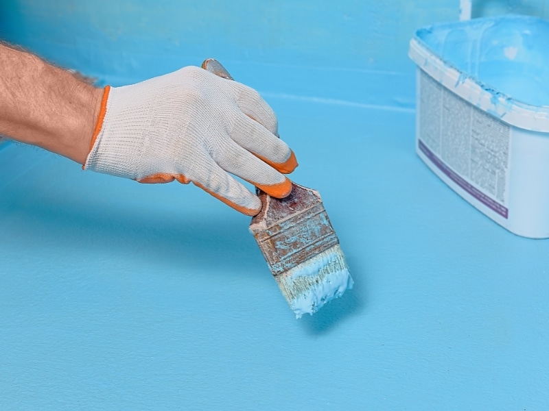 A person applying waterproofing to a bathroom floor ensures effective moisture protection and durability for the bathroom surface.