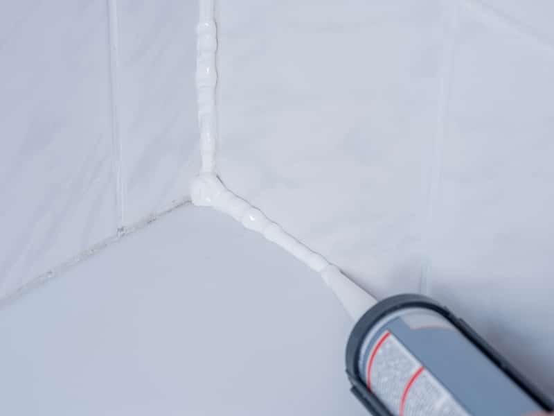 A bloke applies sealant in shower corner where tiles meet the shower base.