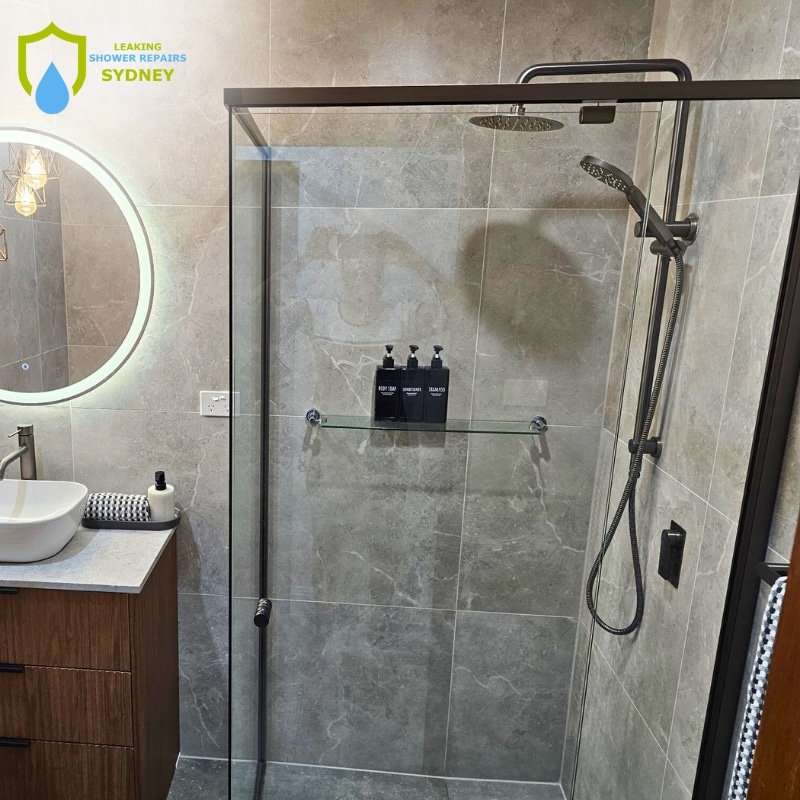 Modern bathroom featuring a glass shower, sleek sink, and elegant lighting with stone tiles and neatly arranged toiletries—perfect for highlighting expert leaking shower repairs in West Gosford by trusted provider.